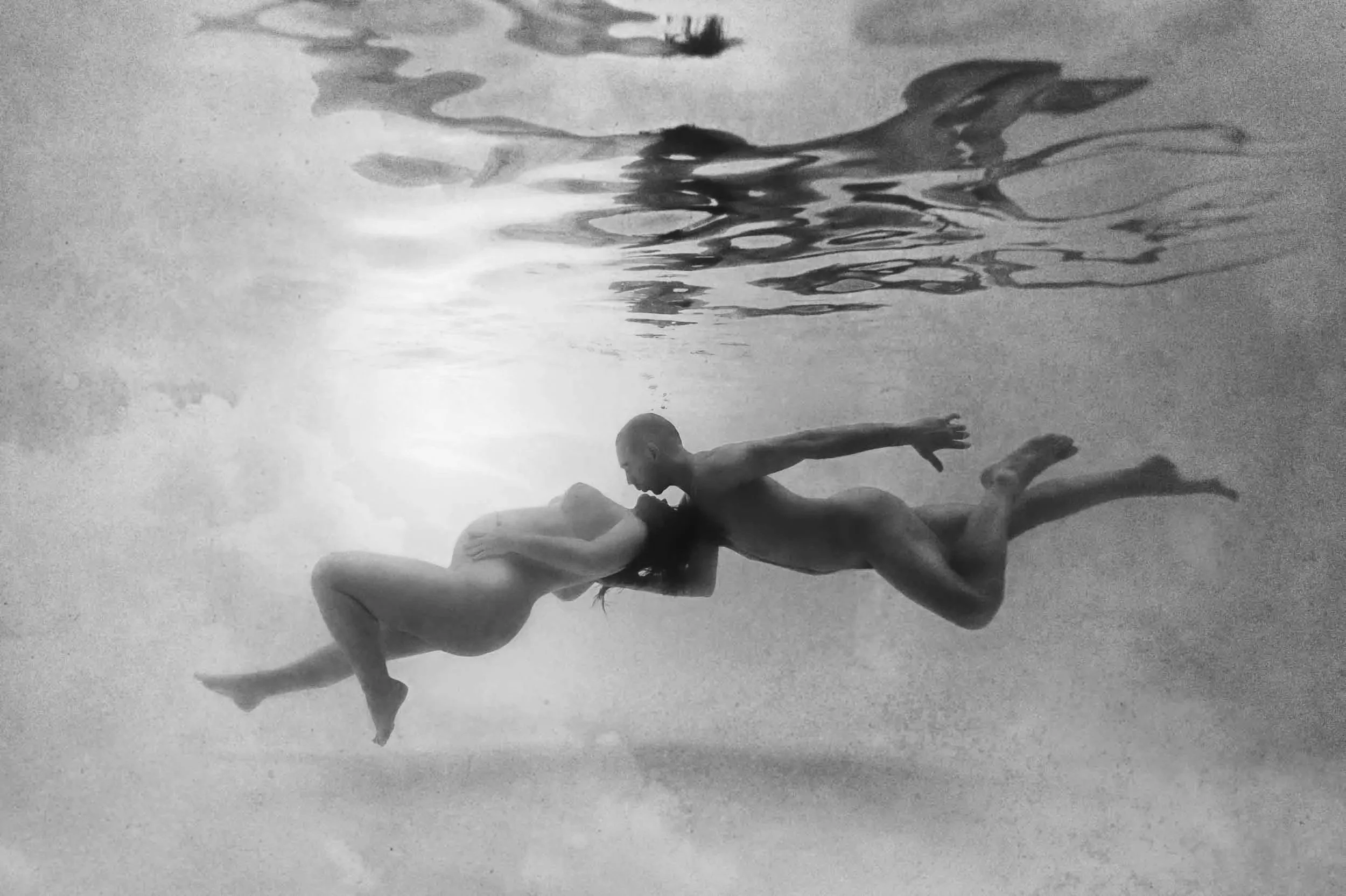 Couple de futur parent photographier sous l'eau en position allongée suspendu dans l'eau en flottaison