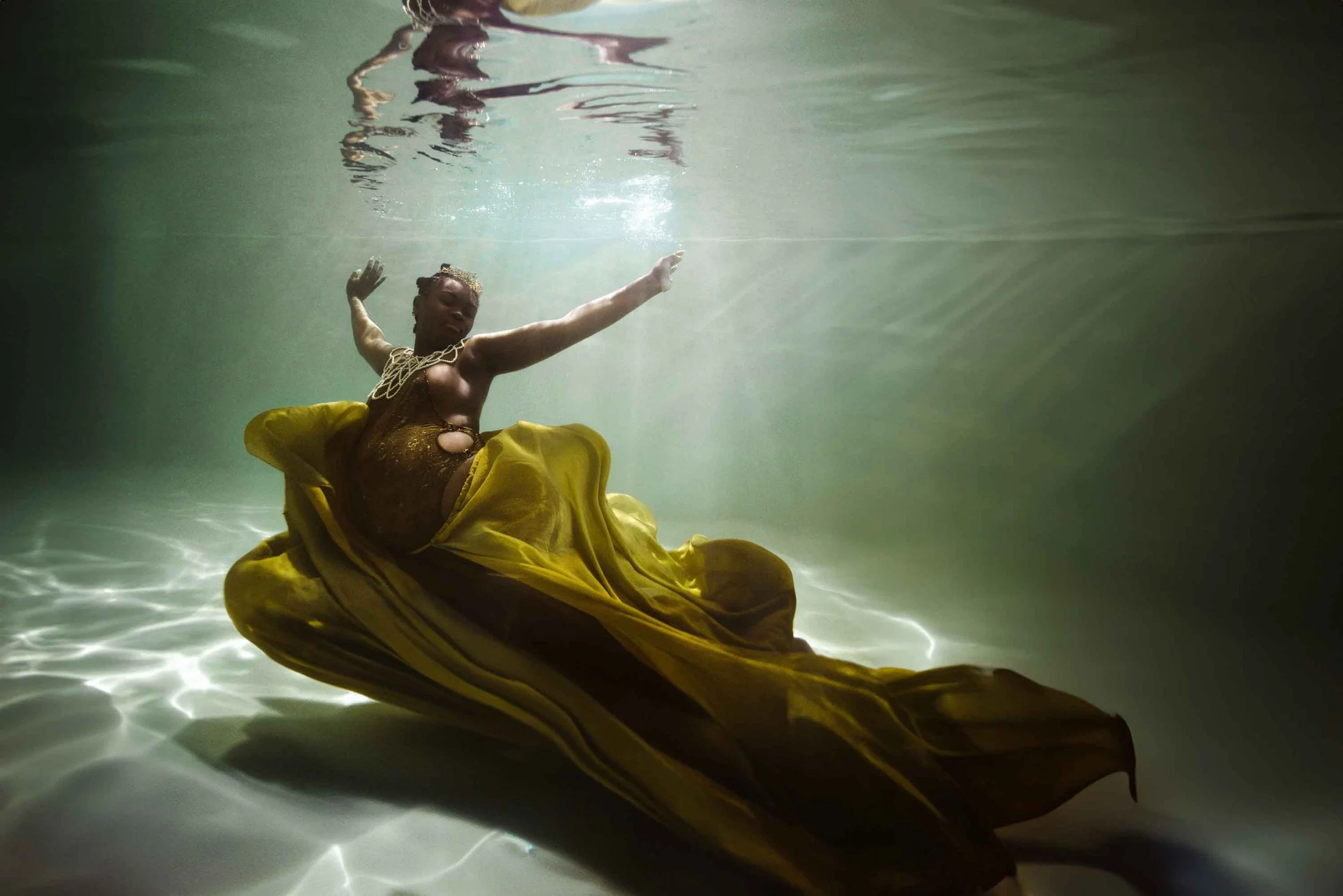 Femme en robe jaune flottant sous l'eau, posant gracieusement dans une piscine ou un environnement aquatique.