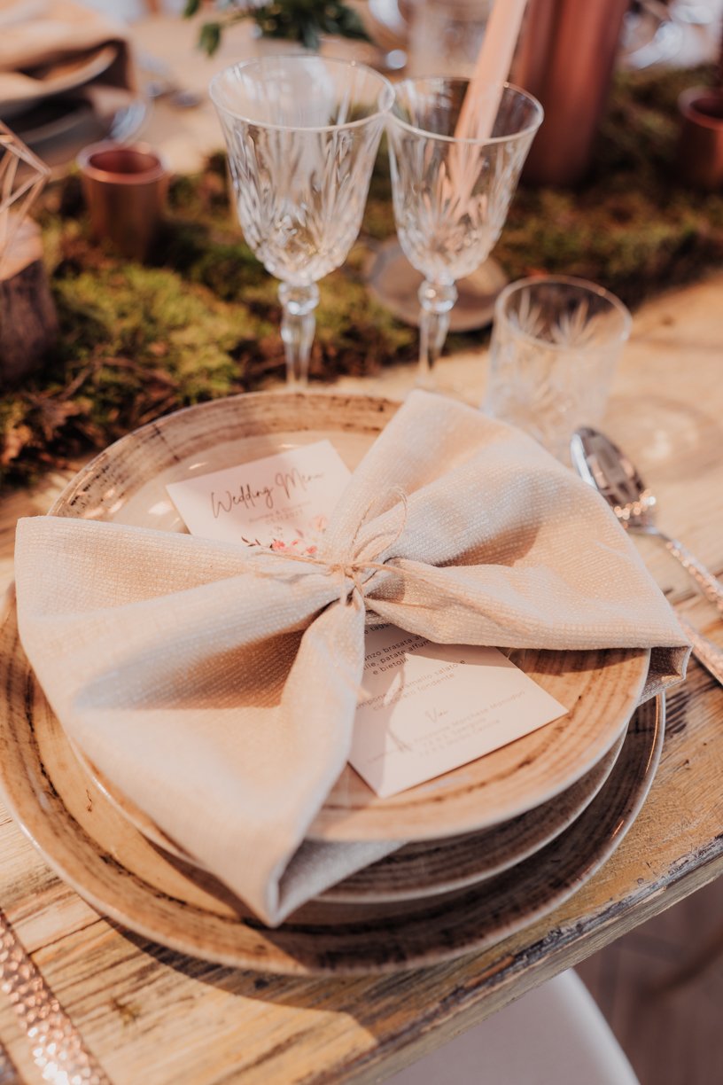 Table setting with plates, folded napkin, menu card, elegant glassware, and rustic decor.