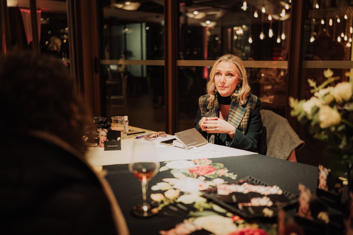 Woman sitting at a table with a notebook and holding a cup in a warmly lit room.