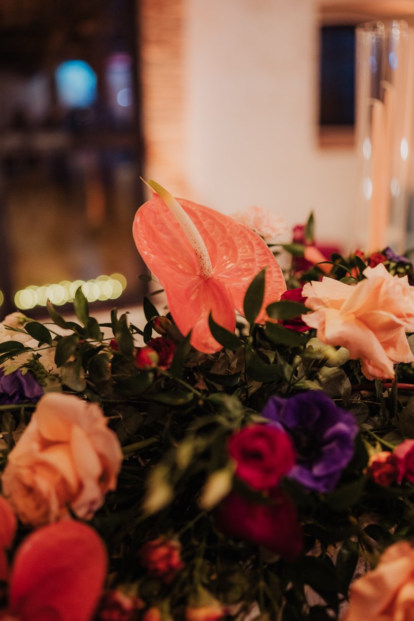 A bouquet featuring a prominent pink anthurium flower surrounded by various colored roses and greenery.