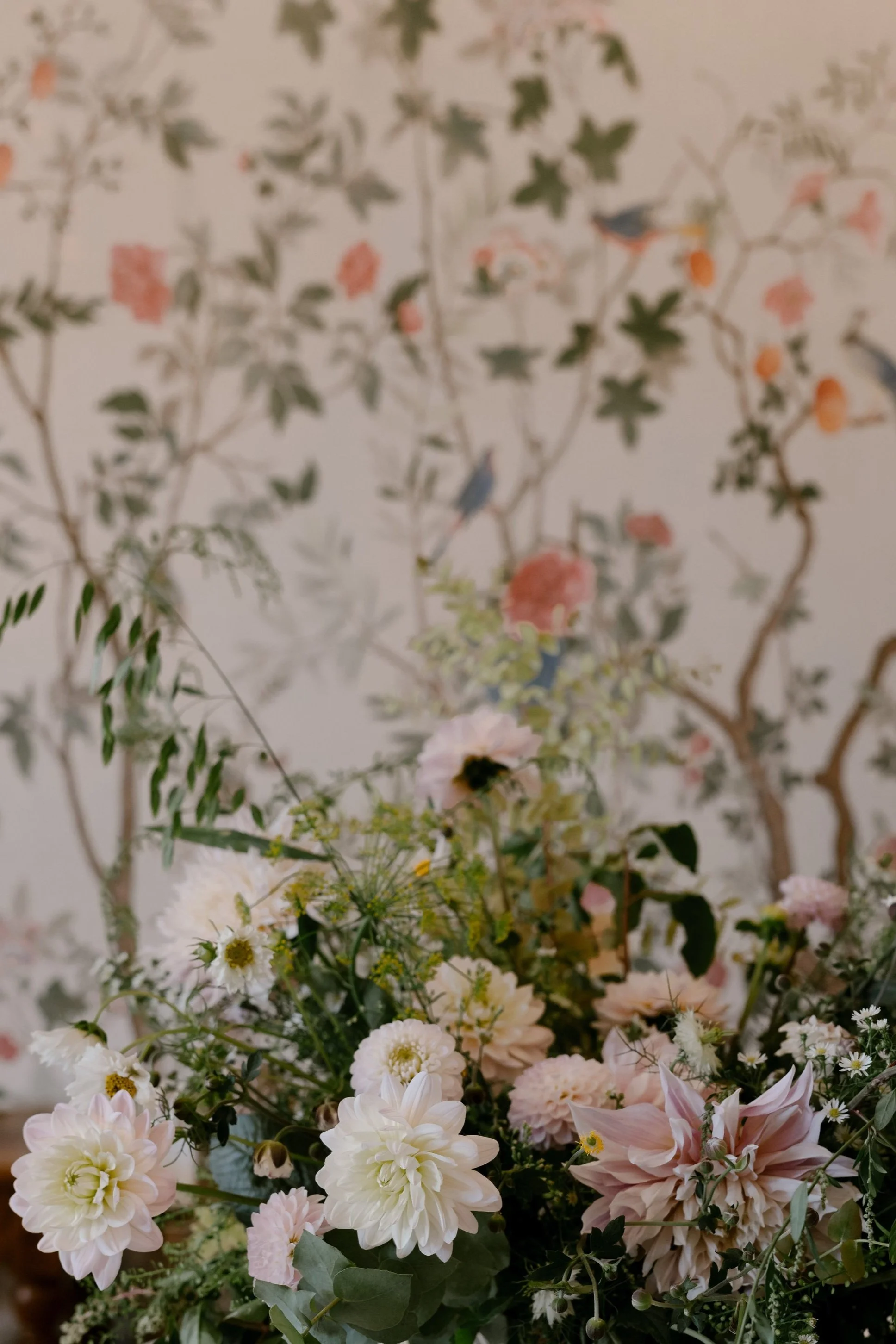 Bouquet of assorted flowers with pink dahlias, greenery, and a blurred floral wallpaper backdrop with birds and branches.