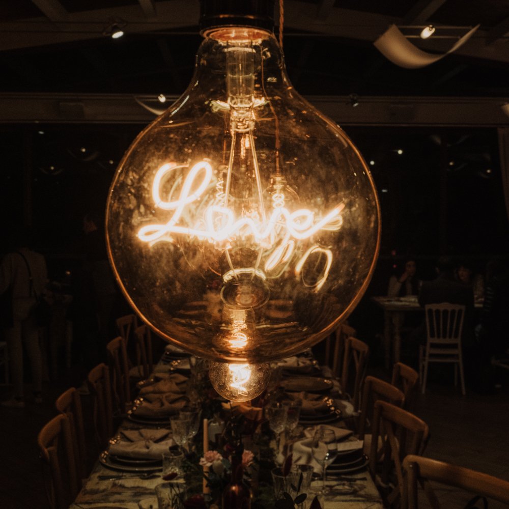 Close-up of a large light bulb with the word "Love" illuminated inside, hanging over a dining table set for a formal event.