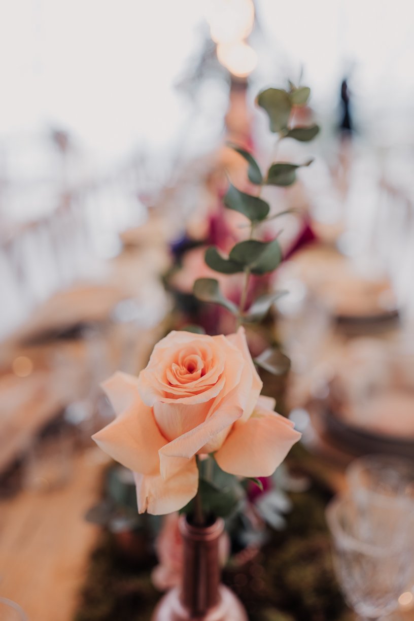Close-up of a peach rose in a vase on a decorated table.