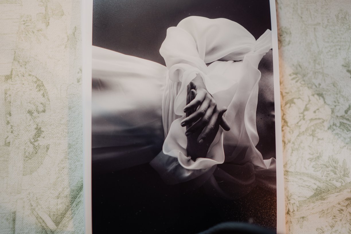 Black and white photo of a person in a flowing white garment, with clasped hands.