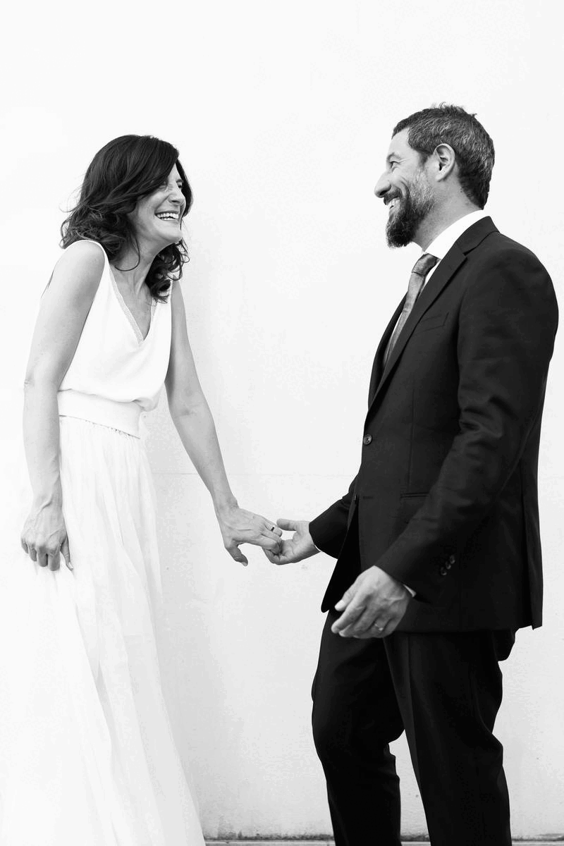 Smiling couple holding hands, woman in a white dress and man in a suit.