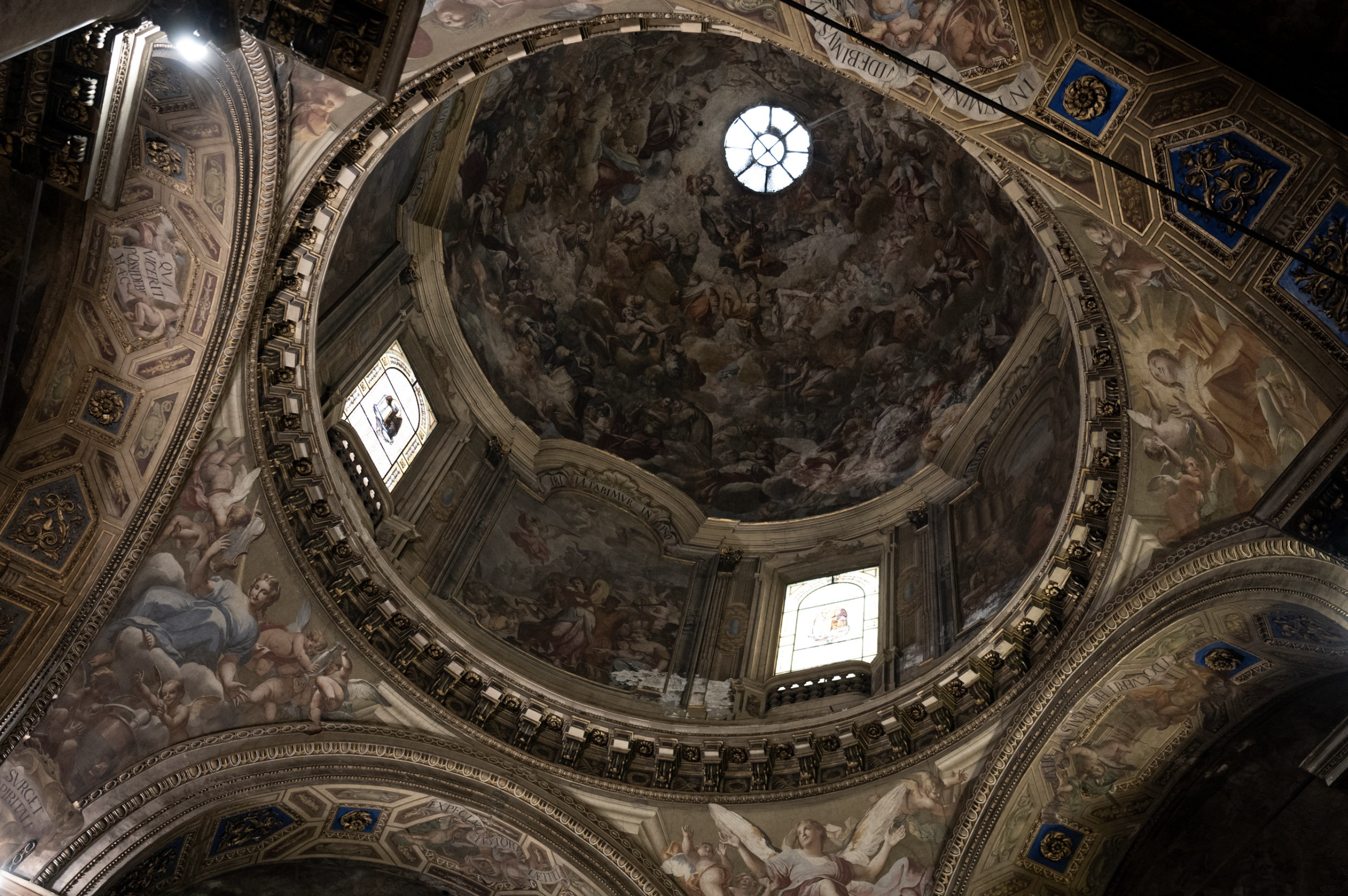 Interior of a domed ceiling with ornate frescoes and a central circular window.