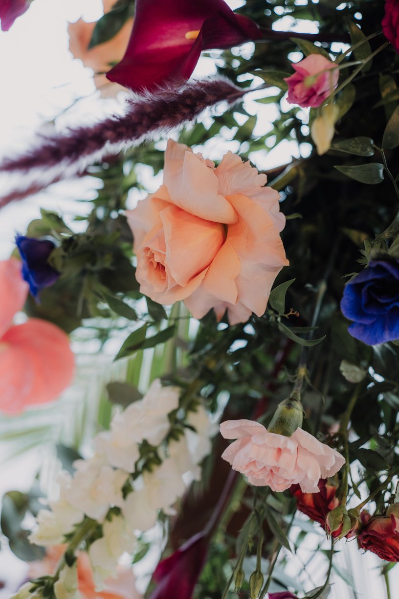 Close-up of a floral arrangement featuring peach roses, pink carnations, blue flowers, and greenery.