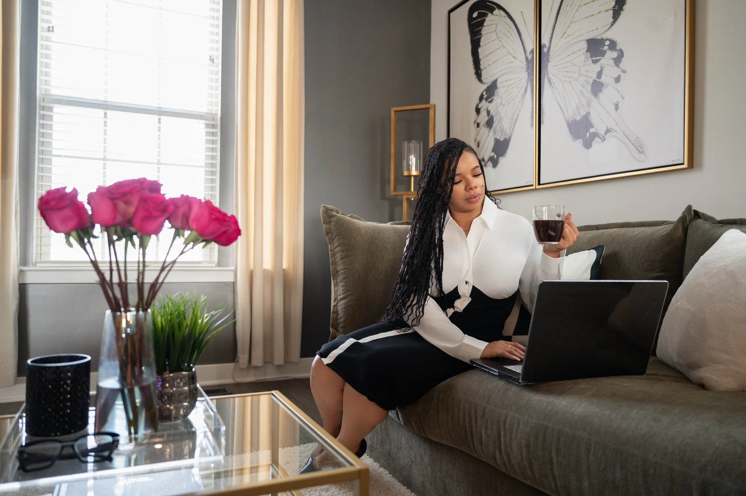 woman sitting on couch holding coffee in one hand while typing with another