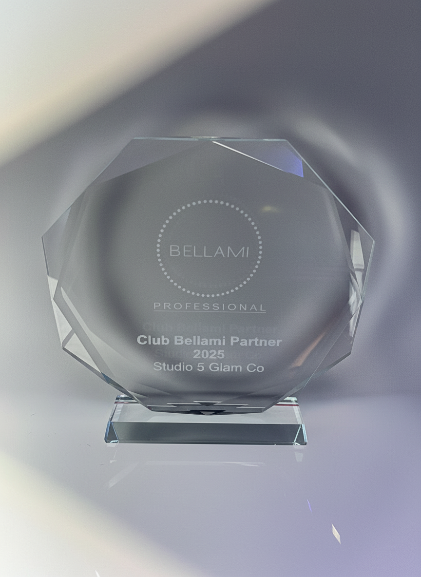 A clear glass trophy with a diamond shape, engraved with the words 'BELLAMI PROFESSIONAL', 'Club Bellami Partner 2025', and 'Studio 5 Glam Co'.