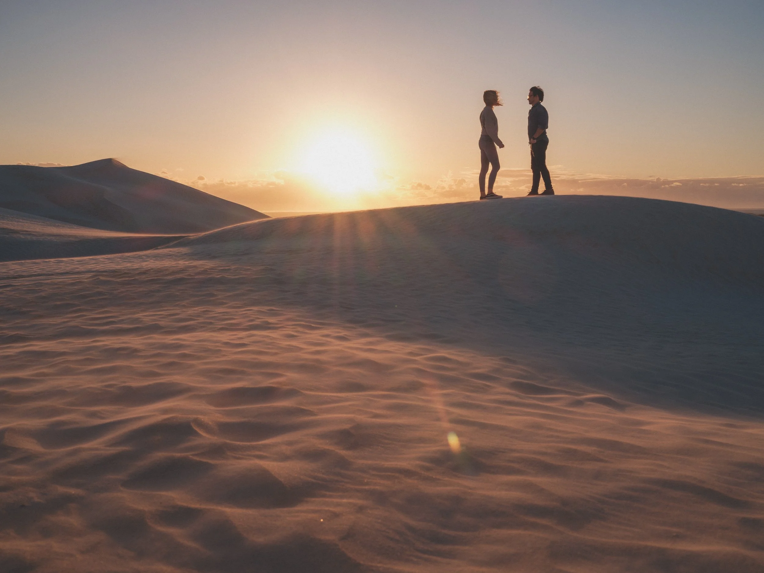 Two visitors standing on the Cervantes sand dunes at sunset.