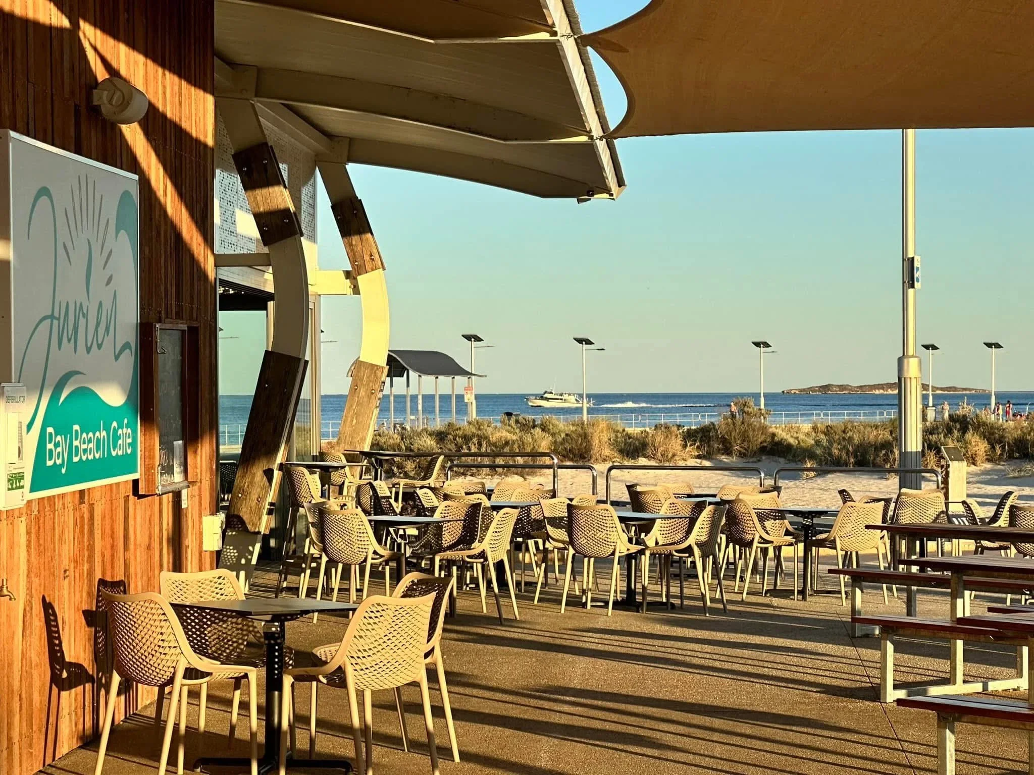 Outdoor seating at Jurien Bay Beach Cafe overing looking Jurien Bay Oceanic Experience's tour vessel going by Jurien Bay, Western Australia.
