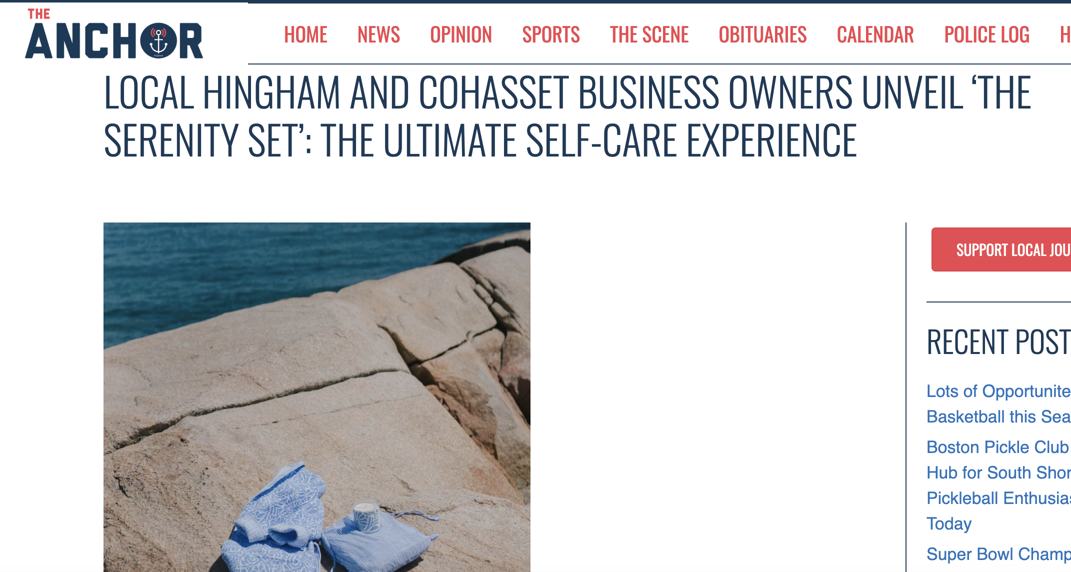 A rocky shoreline with a blue and white cloth and a small candle on the rocks, overlooking the water.