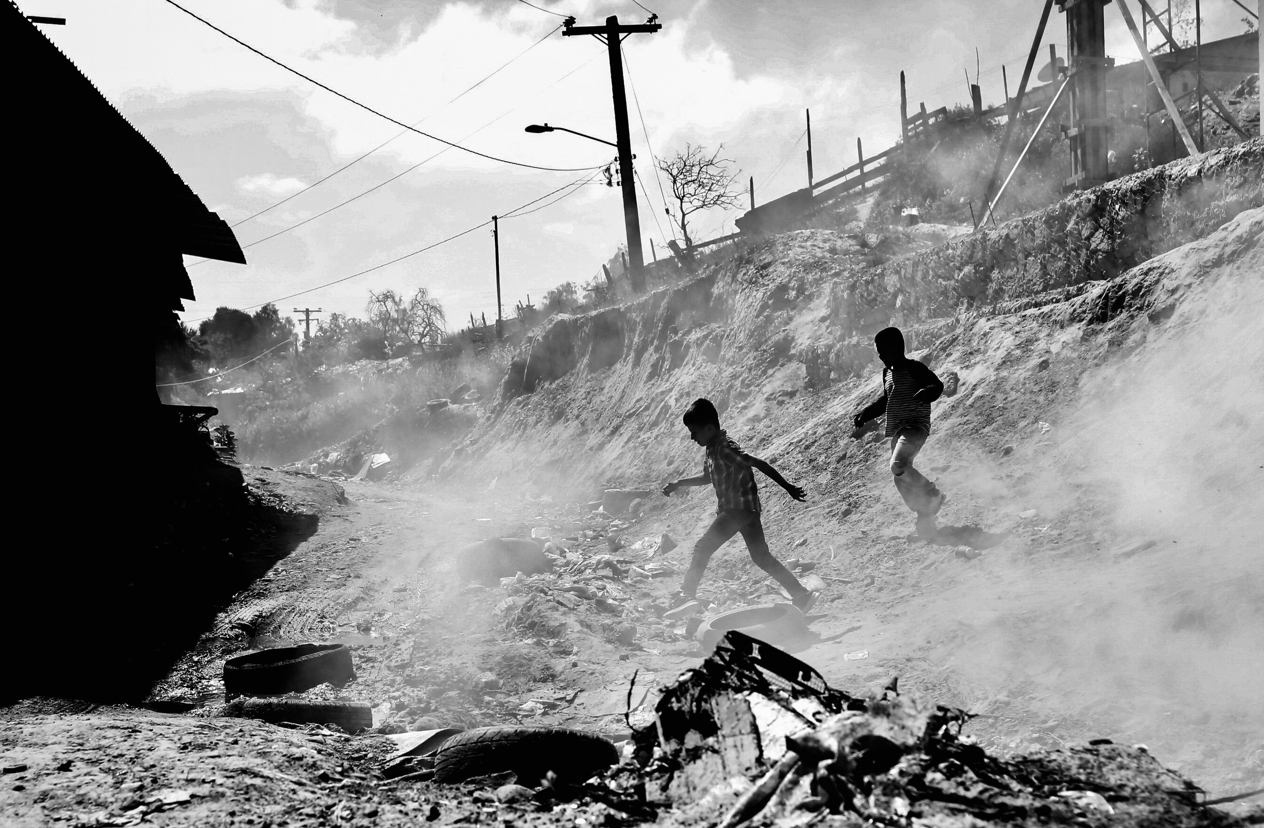  Two boys play in between piles of burning trash outside Embajadores de Jesus, a migrant shelter in Tijuana, Mexico. 
