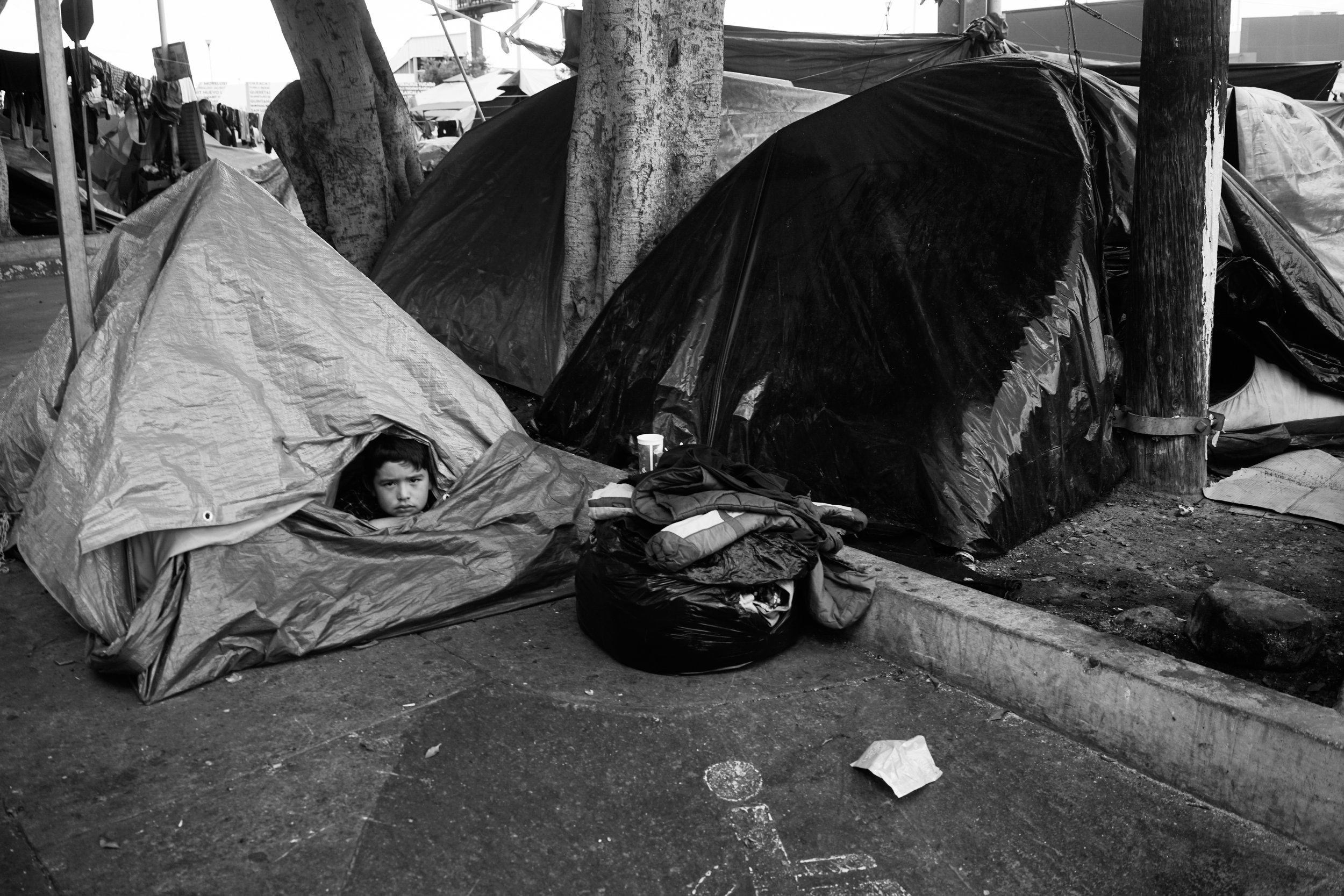  A boy looks out of his tent and current home at El Chaparral in Tijuana, Mexico. 