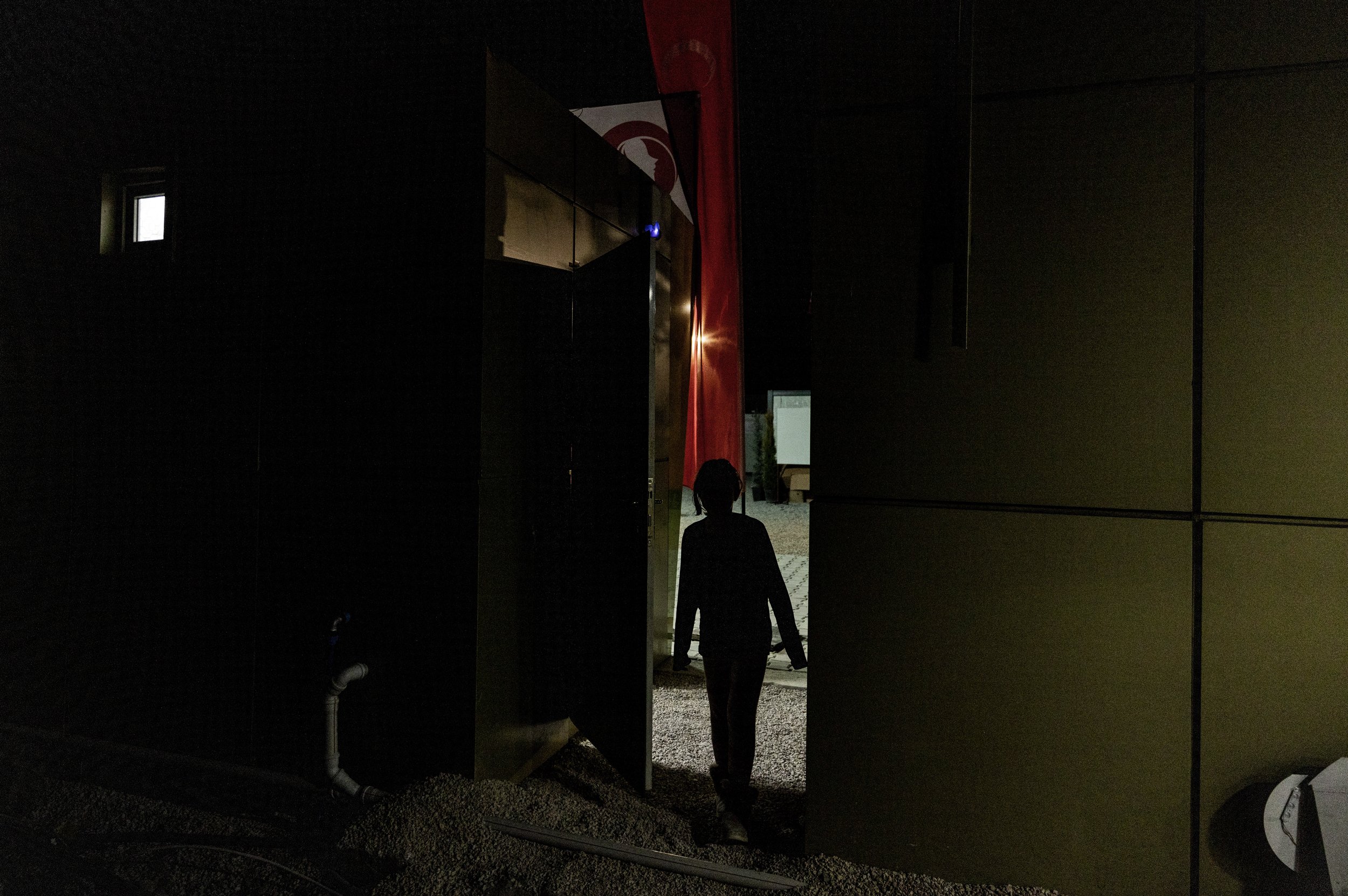  A young female refugee is silhouetted in the shadows with the Turkish flag in the background. 