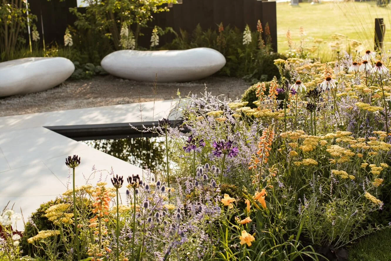 A garden with colorful flowers, a reflective pond, and modern white stone sculptures.