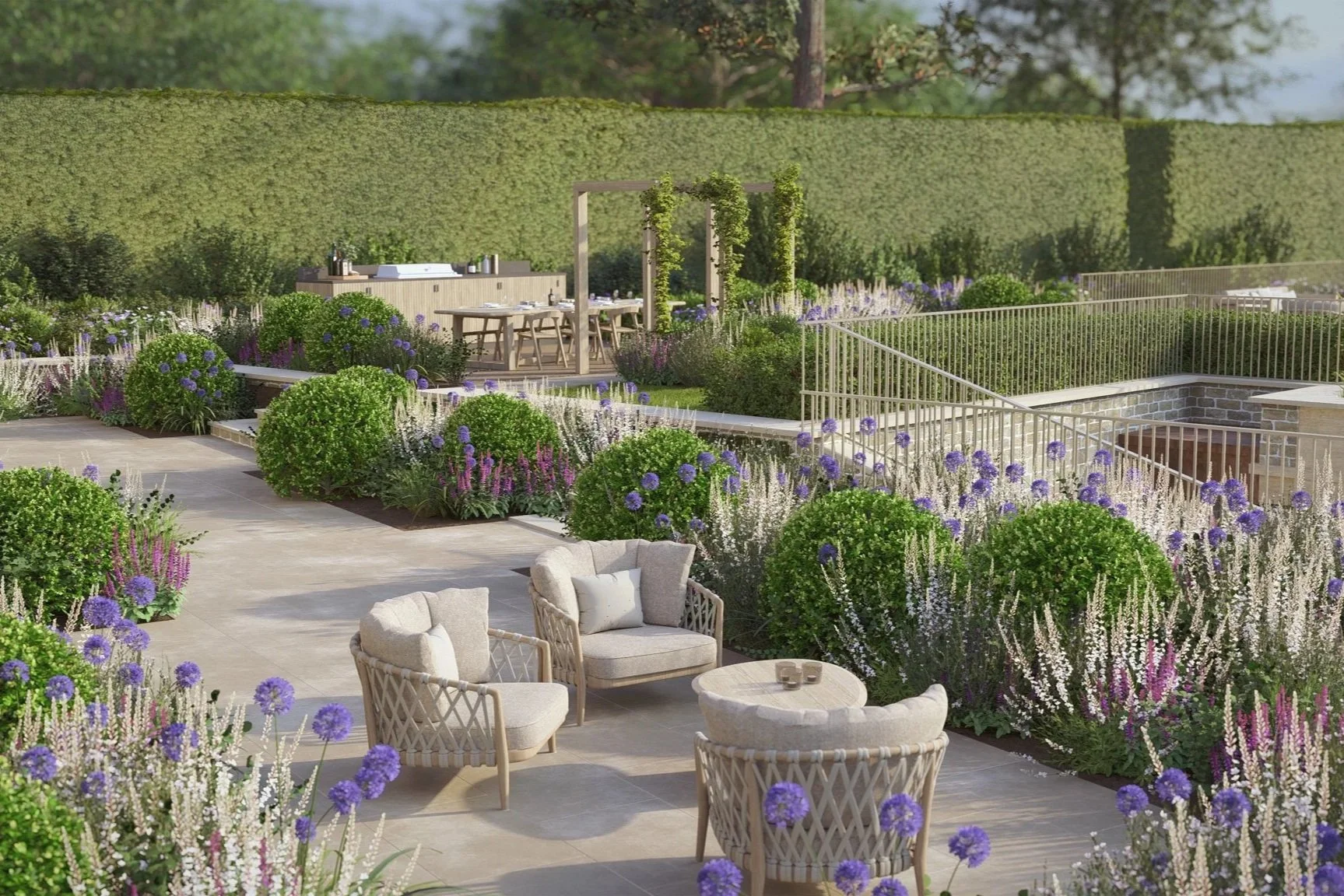 A beautifully landscaped outdoor patio with lounge chairs and a small table surrounded by vibrant purple, white, and green flowering plants, with a garden dining area in the background and lush green hedges