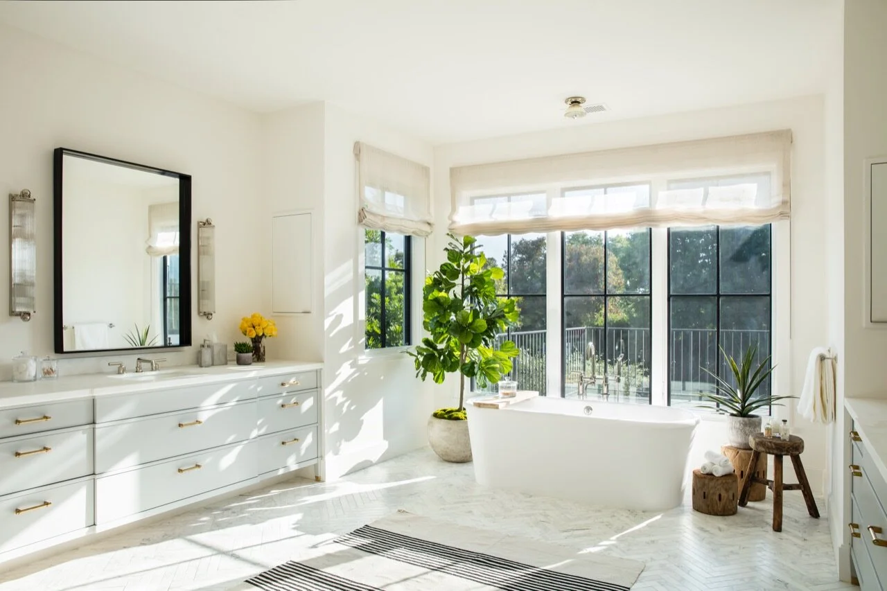 Master bathroom with rug, sconces, fig tree, stools, herringbone tile floors, urban electric and linen roman shades. 