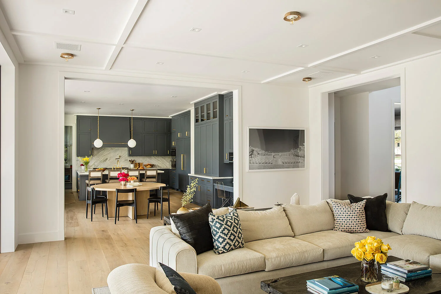 Custom sectional sofa, wide plank, white oak floors, pillows, dark kitchen. 