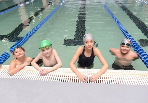 Four young children posing on the side of the pool