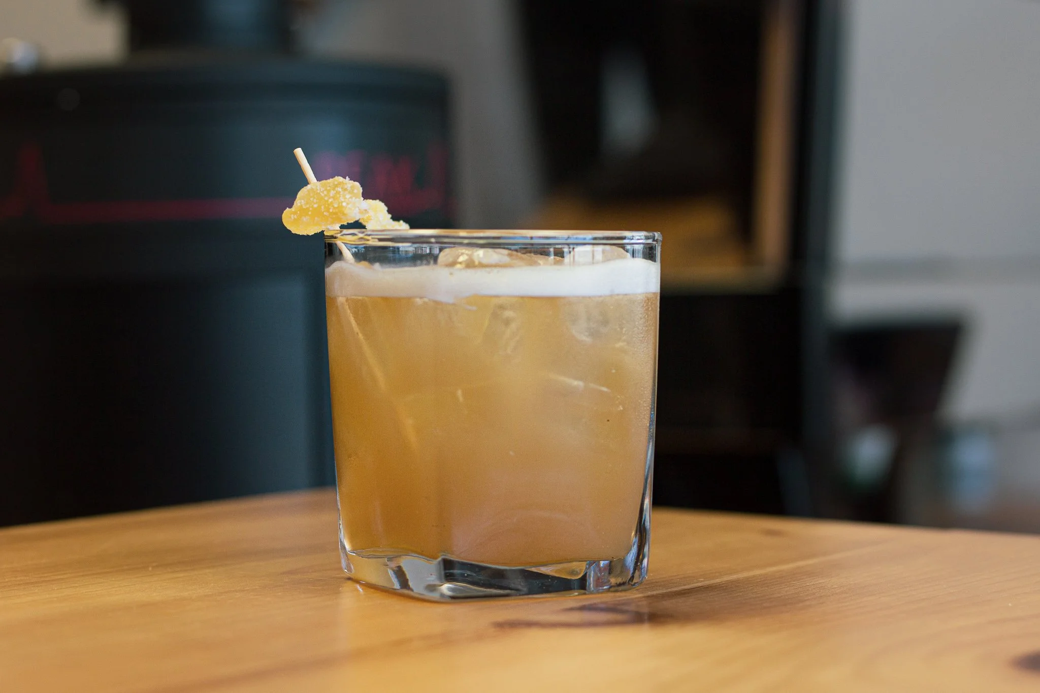 A glass of iced yellowish cocktail garnished with a sugar-coated lemon slice on a wooden table.