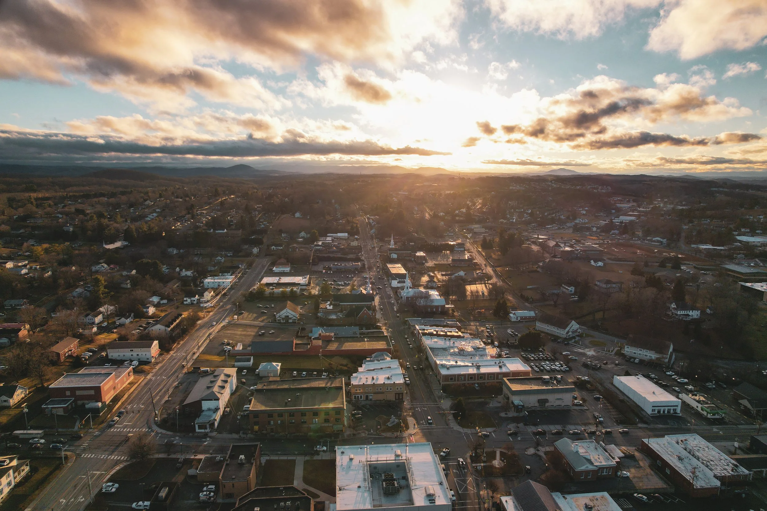 An aerial view of a small town during sunset with buildings, streets, and a church with a tall steeple.