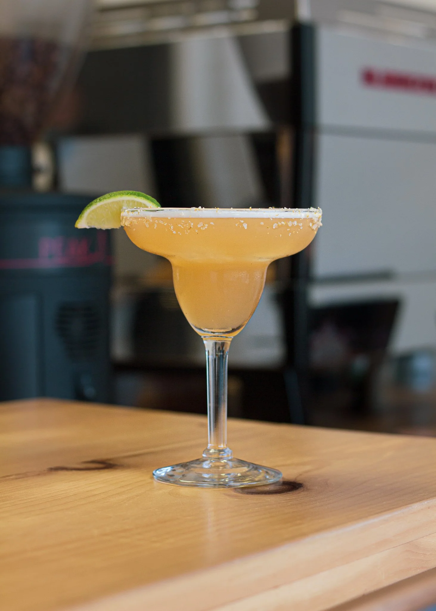 A margarita cocktail in a glass with a salted rim and a lime wedge on the edge, placed on a wooden surface.