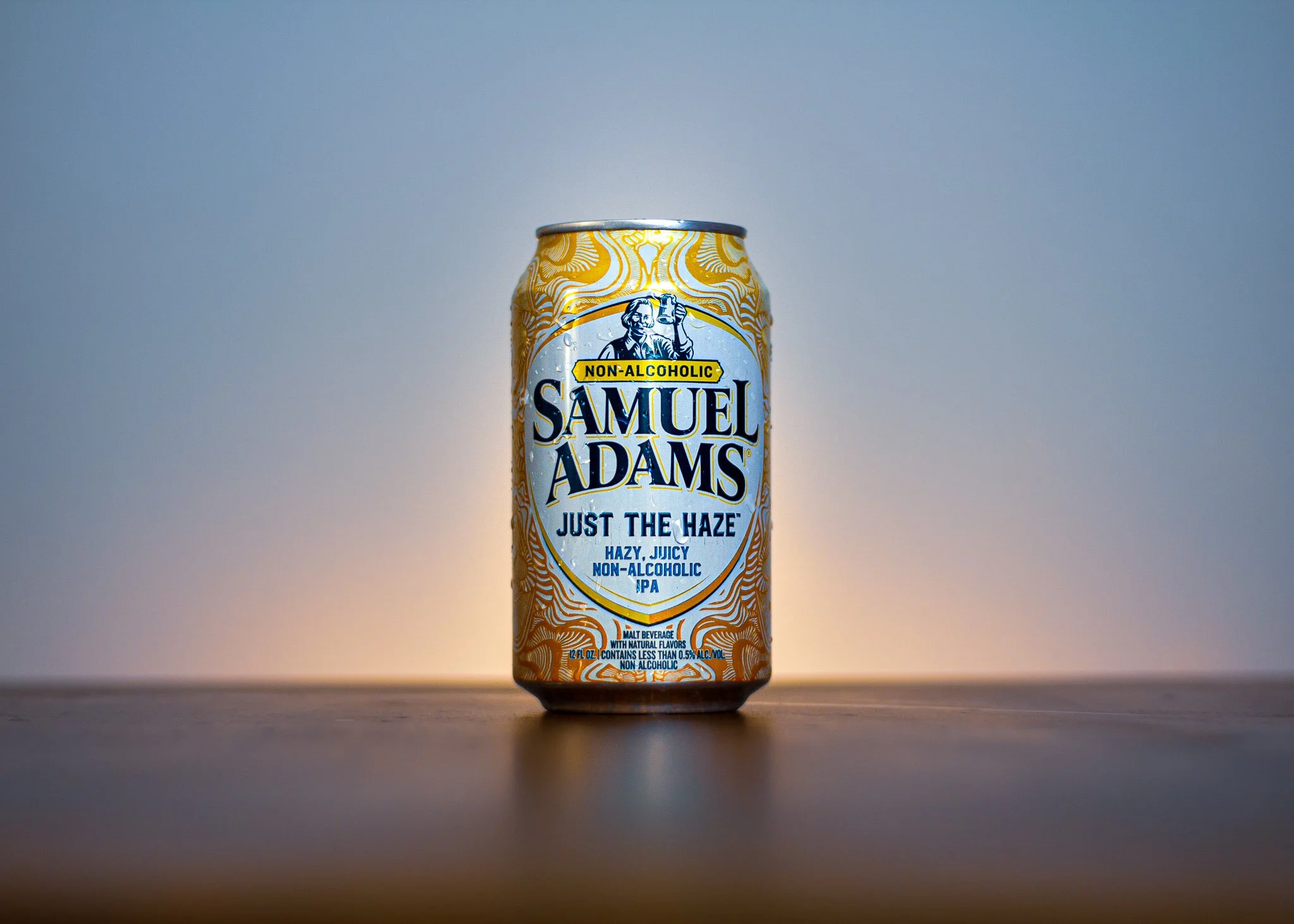 Can of Samuel Adams Just the Haze non-alcoholic IPA positioned on a wooden surface with a gradient background.