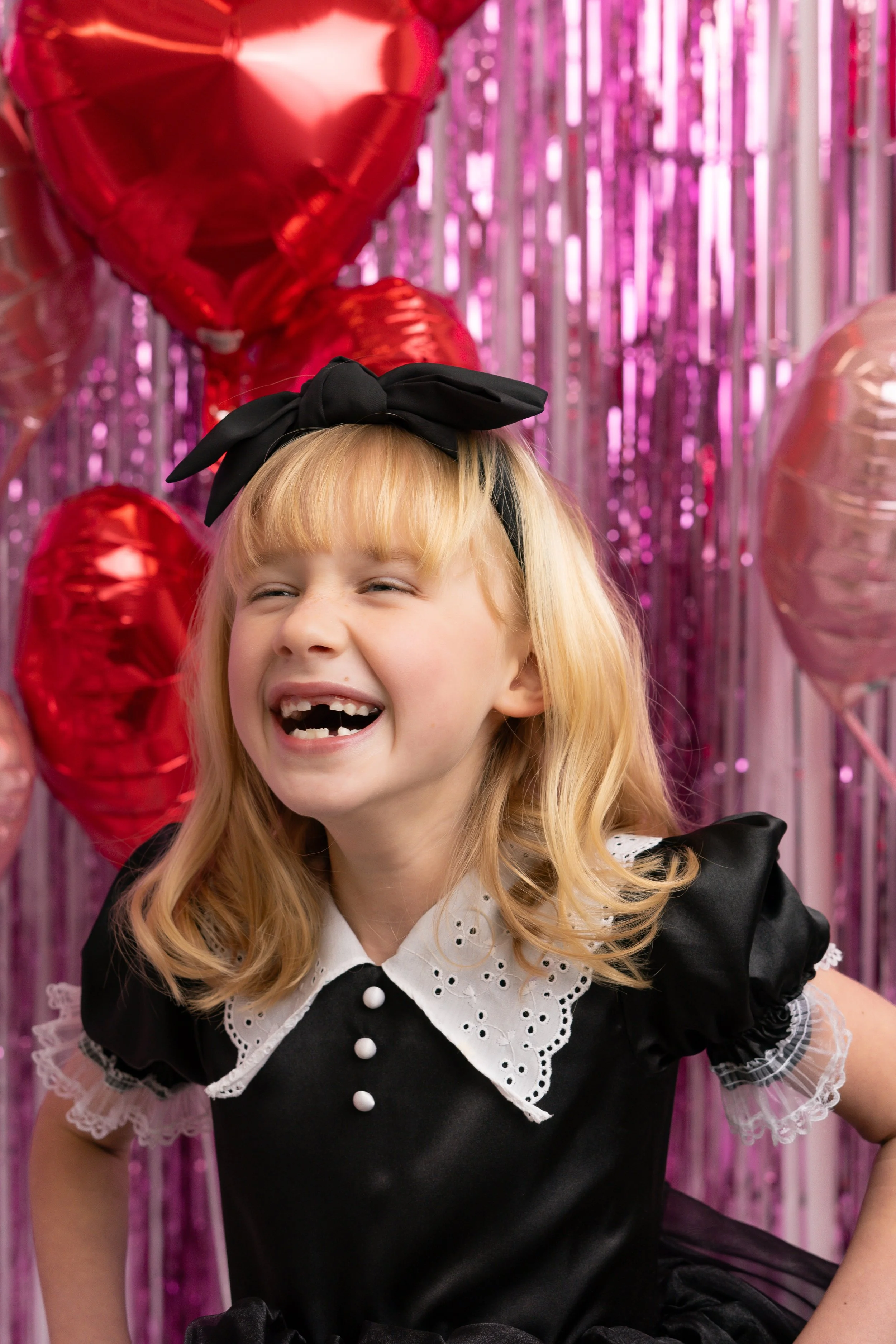Smiling child in black dress and bow with heart balloons