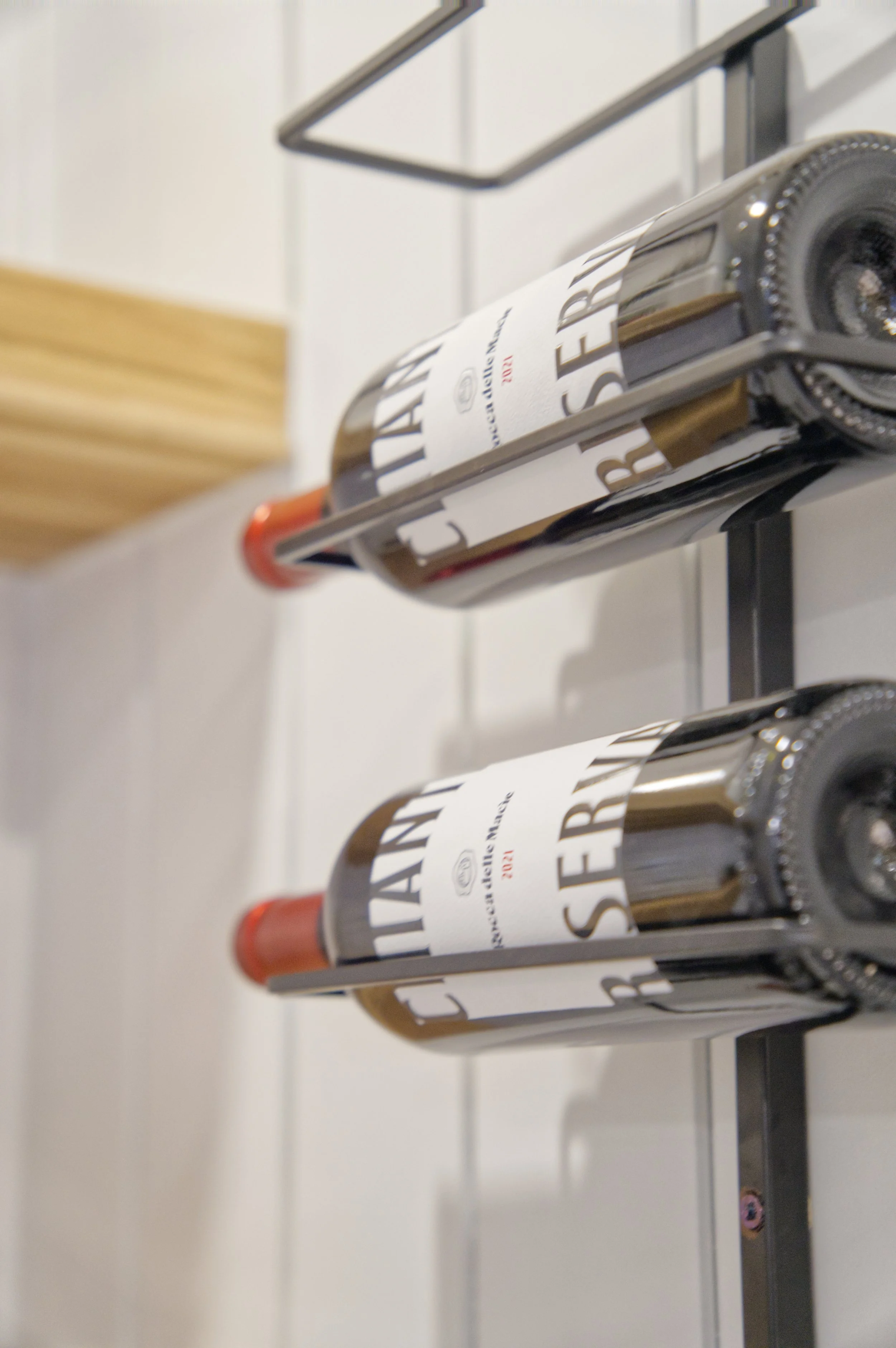 Two bottles of salad dressing on a metal rack, with white background and a wooden block on the left.