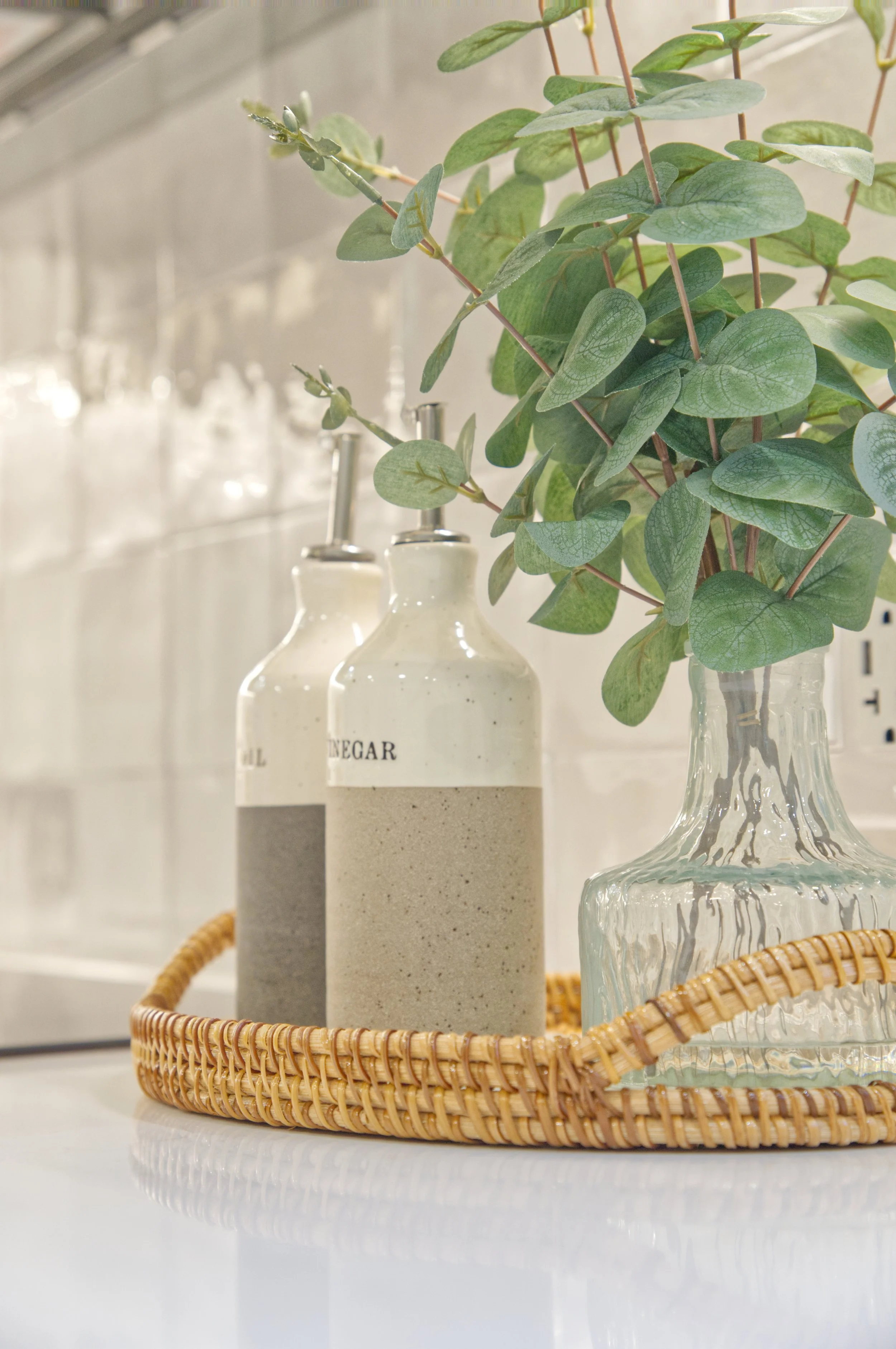 A wicker tray holding a glass vase with greenery and two ceramic bottles.