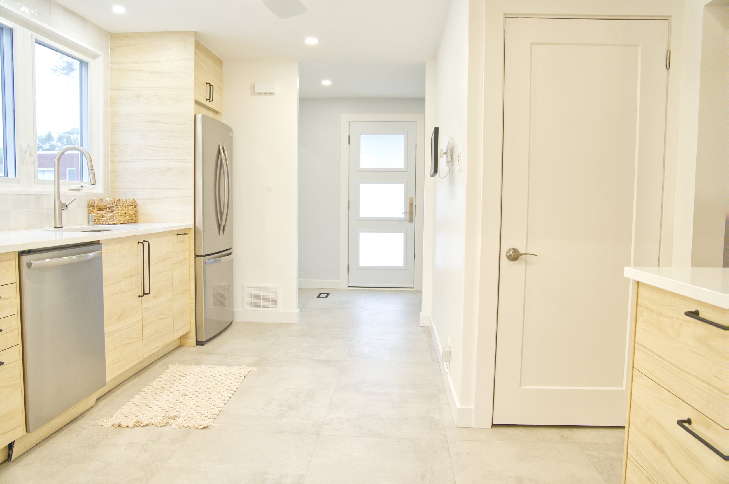 Bright, modern kitchen with light wood cabinets, stainless steel appliances, a window above the sink, and a door at the back with three square frosted glass panels.