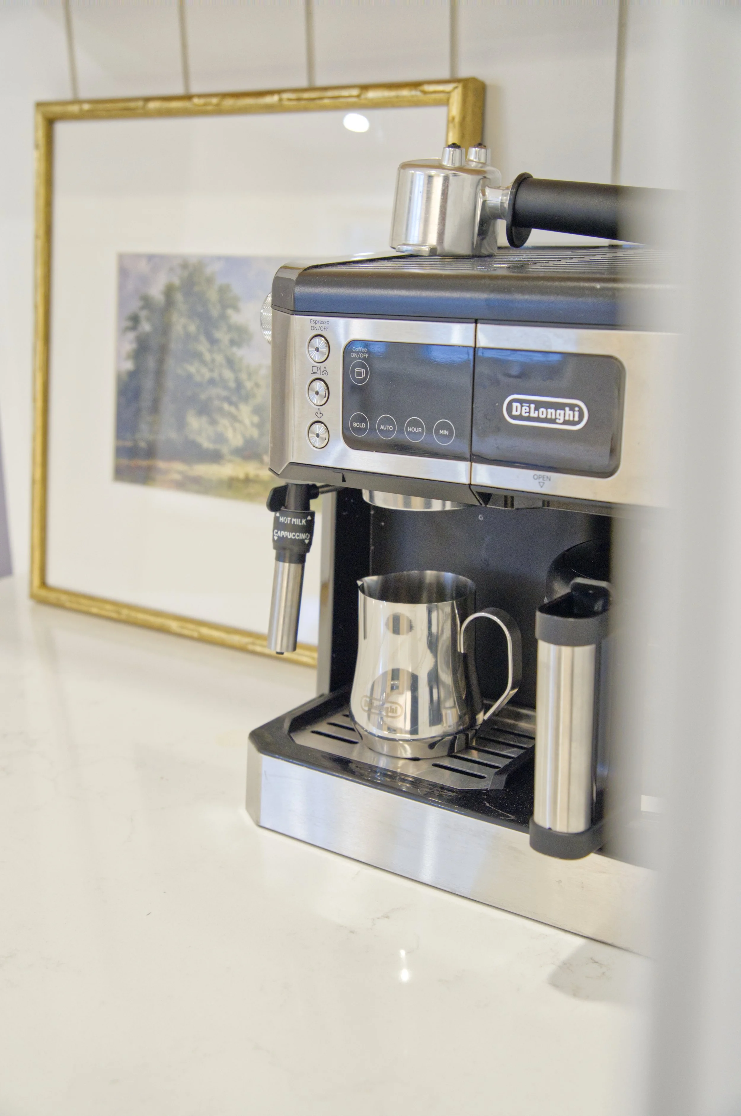 Stainless steel DeLonghi espresso machine with a metal milk frothing pitcher on the drip tray.