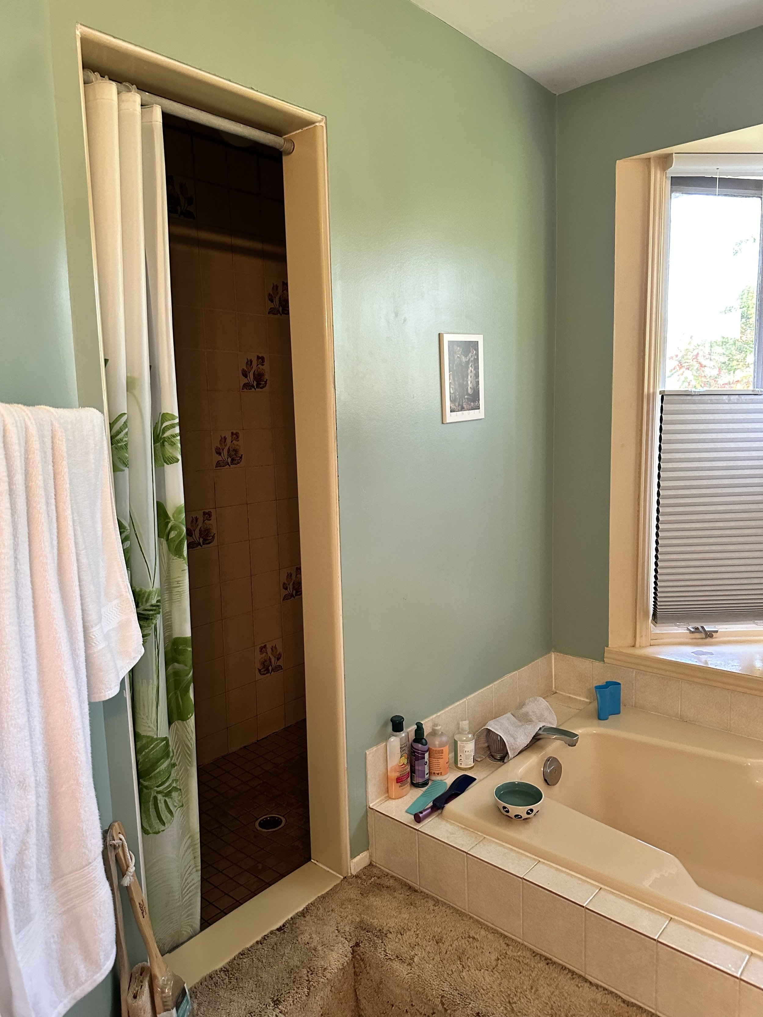 Bathroom with a bathtub, a window, and a shower area with a curtain. Several toiletries are placed on the edge of the tub and a towel hangs on a rack.