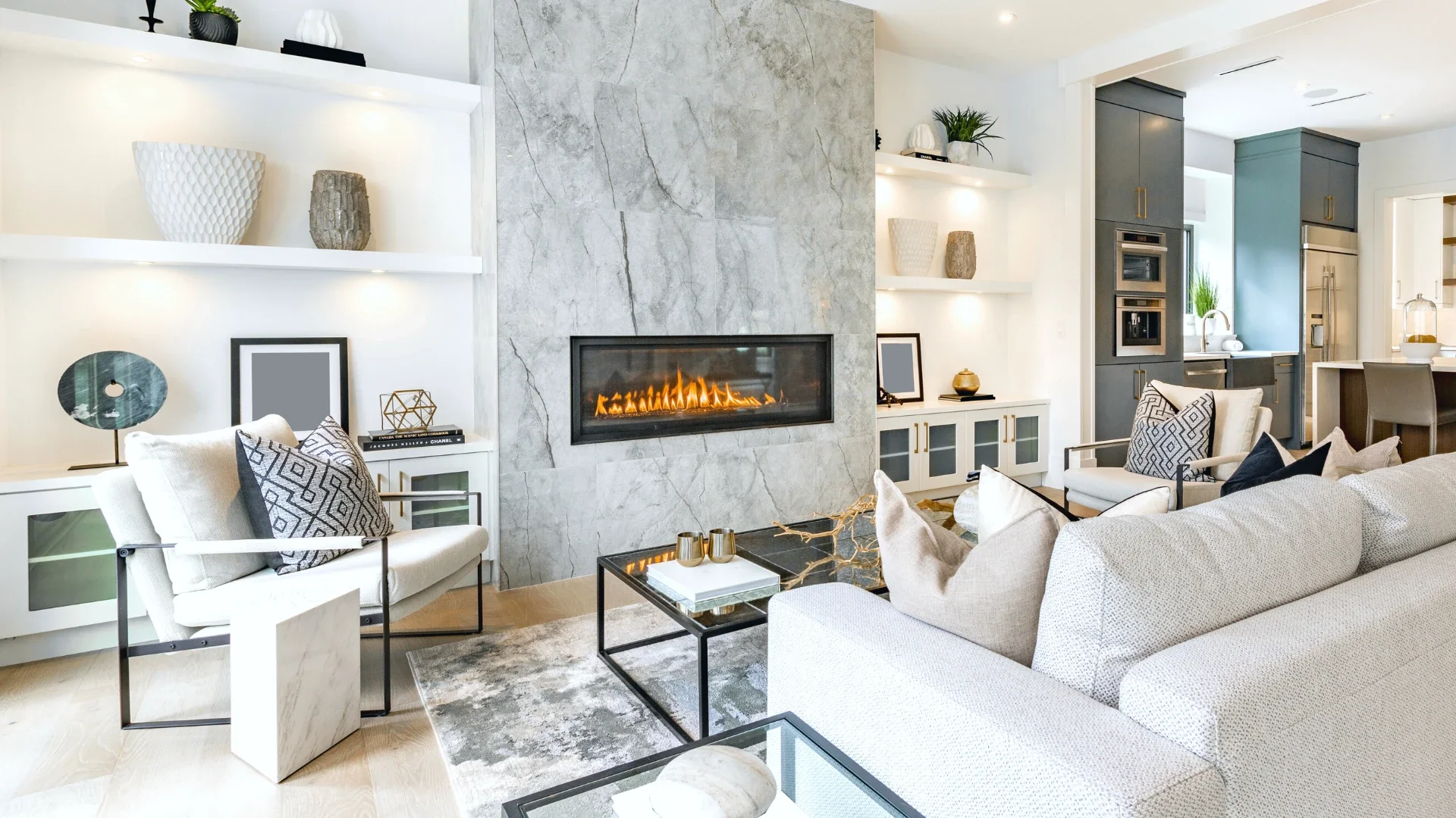 Living room with modern decor, featuring a fireplace, white sofas, armchairs with patterned pillows, and built-in shelves with decorative items.