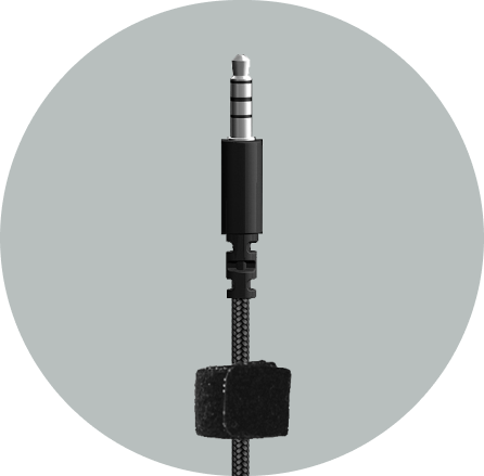 Close-up of the AC-6008 silver three-band 3.5mm plug with a strain-relief boot on a braided cable and hook-and-loop strap in a gray circle — steel-rod-reinforced connector on a 3.5mm headset for schools
