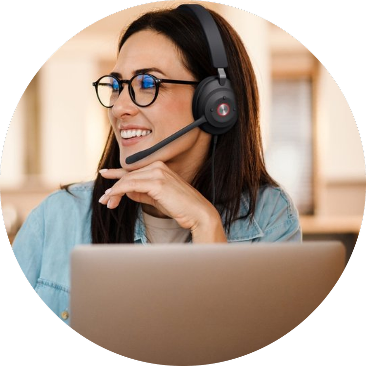 A woman with glasses and a denim jacket smiling while wearing a black headset with a microphone in an office