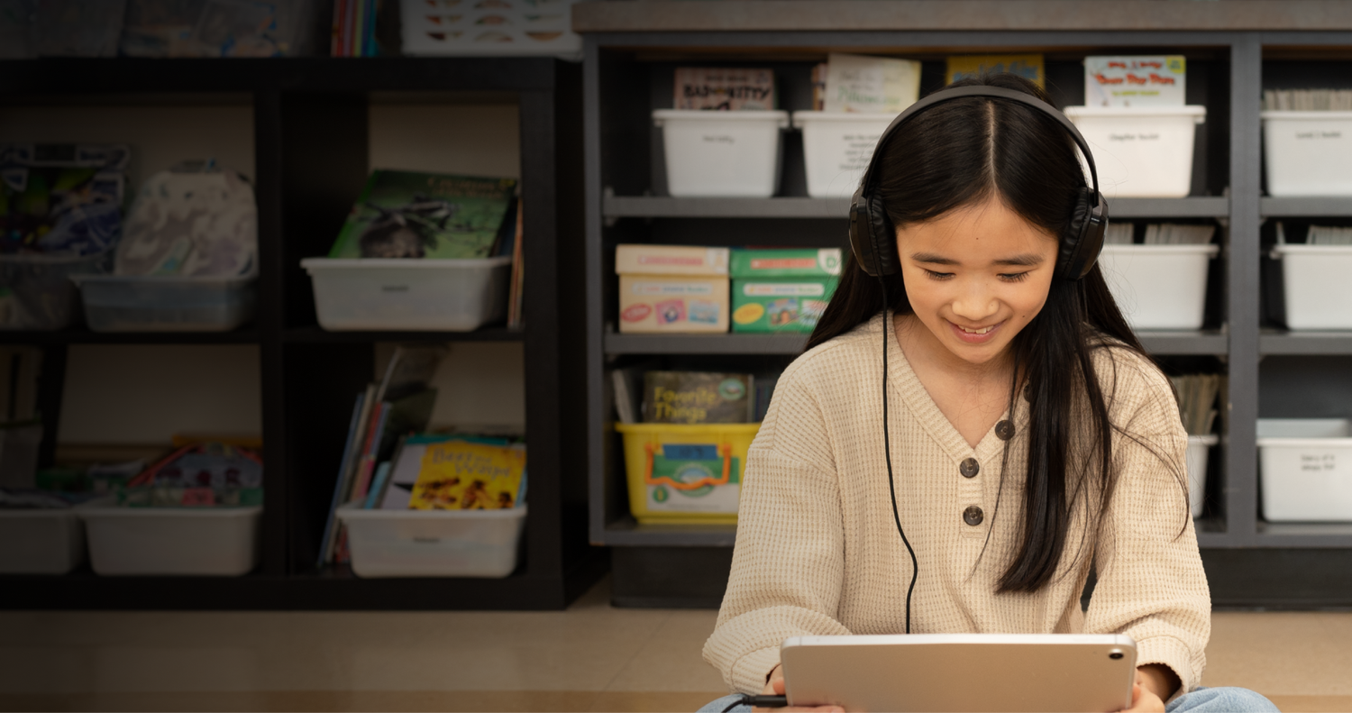 Student wearing headphones smiling while working on a laptop in a classroom