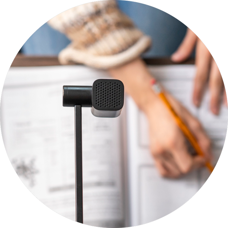 Close-up of a black desktop microphone in front of a person writing in a notebook