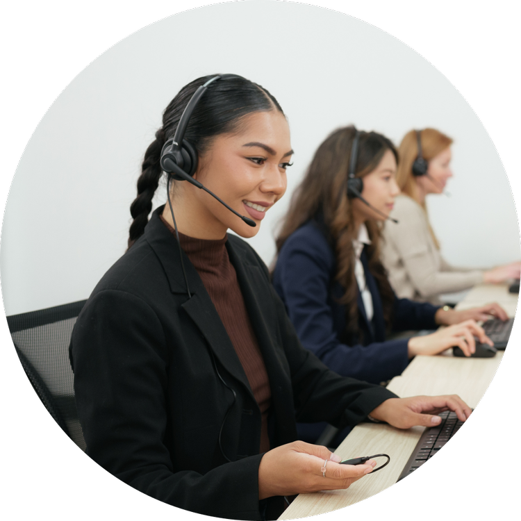 Three women in an office, wearing headsets and working on computers.