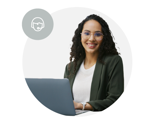 A woman with curly hair and glasses smiling at the camera, sitting at a desk with a laptop, with a headset icon overhead.