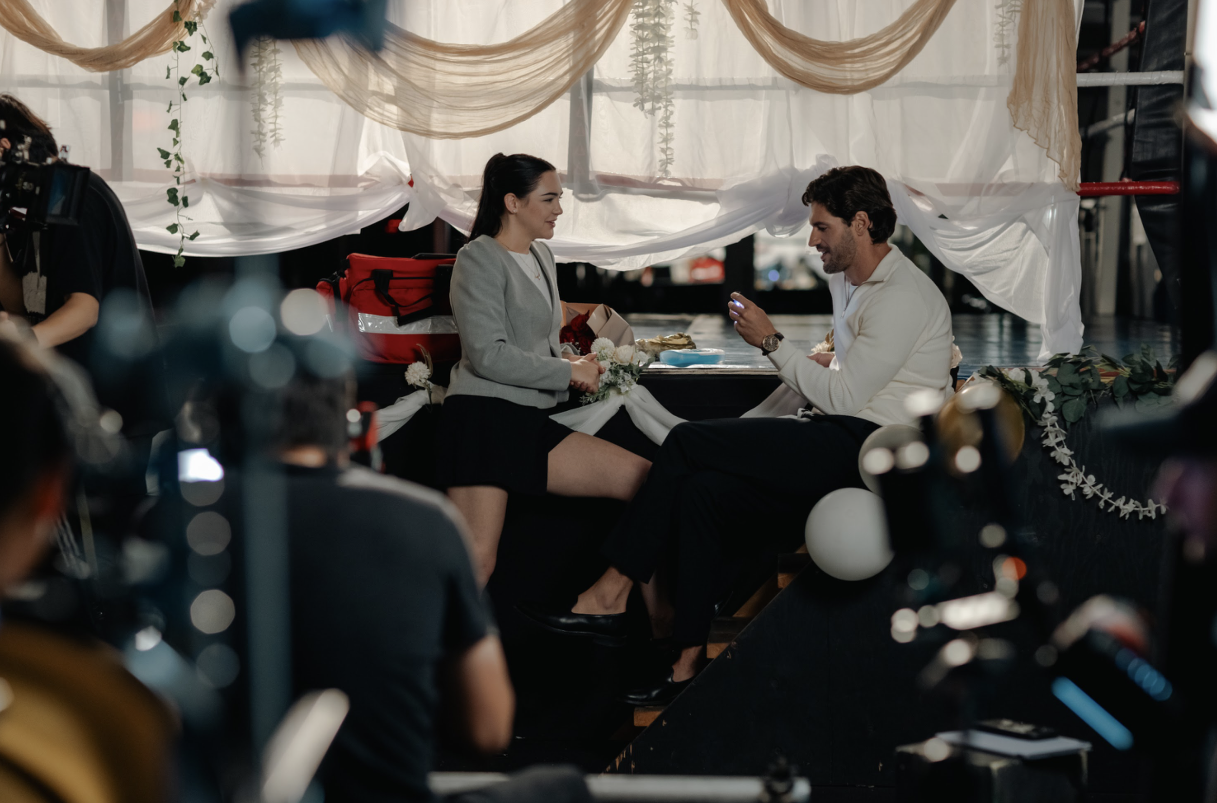 A man and woman having a romantic moment on a boat, with cameras and crew filming around them.