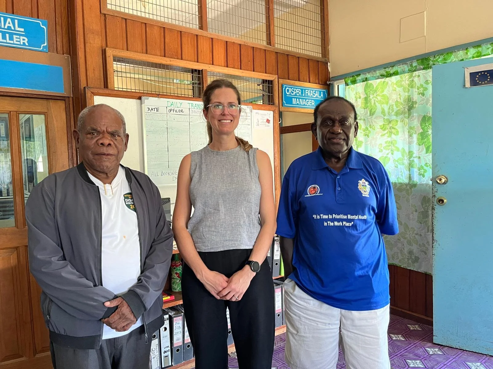 Three people stand together inside an office: two Solomon Islands health representatives on either side of a FEiA team member in the centre.