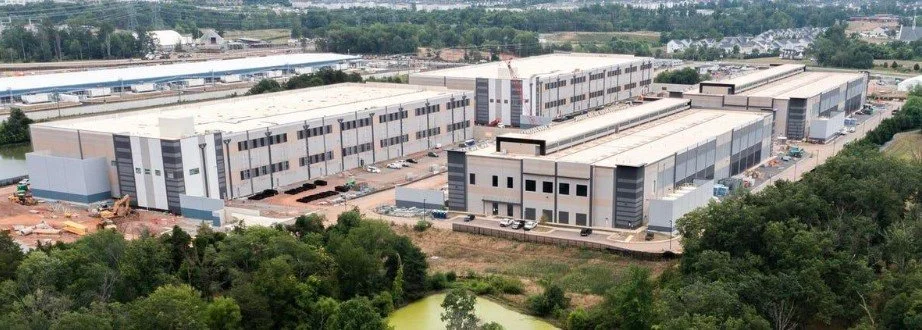 A large industrial warehouse complex with multiple connected buildings, surrounded by trees and a parking lot.