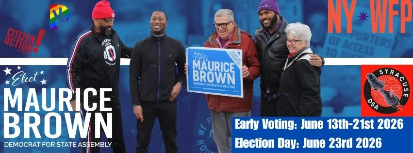 Group of five diverse smiling individuals at a political rally, holding a blue Maurice Brown for County Legislature sign, with campaign banners and logos visible, promoting early voting and election day dates.