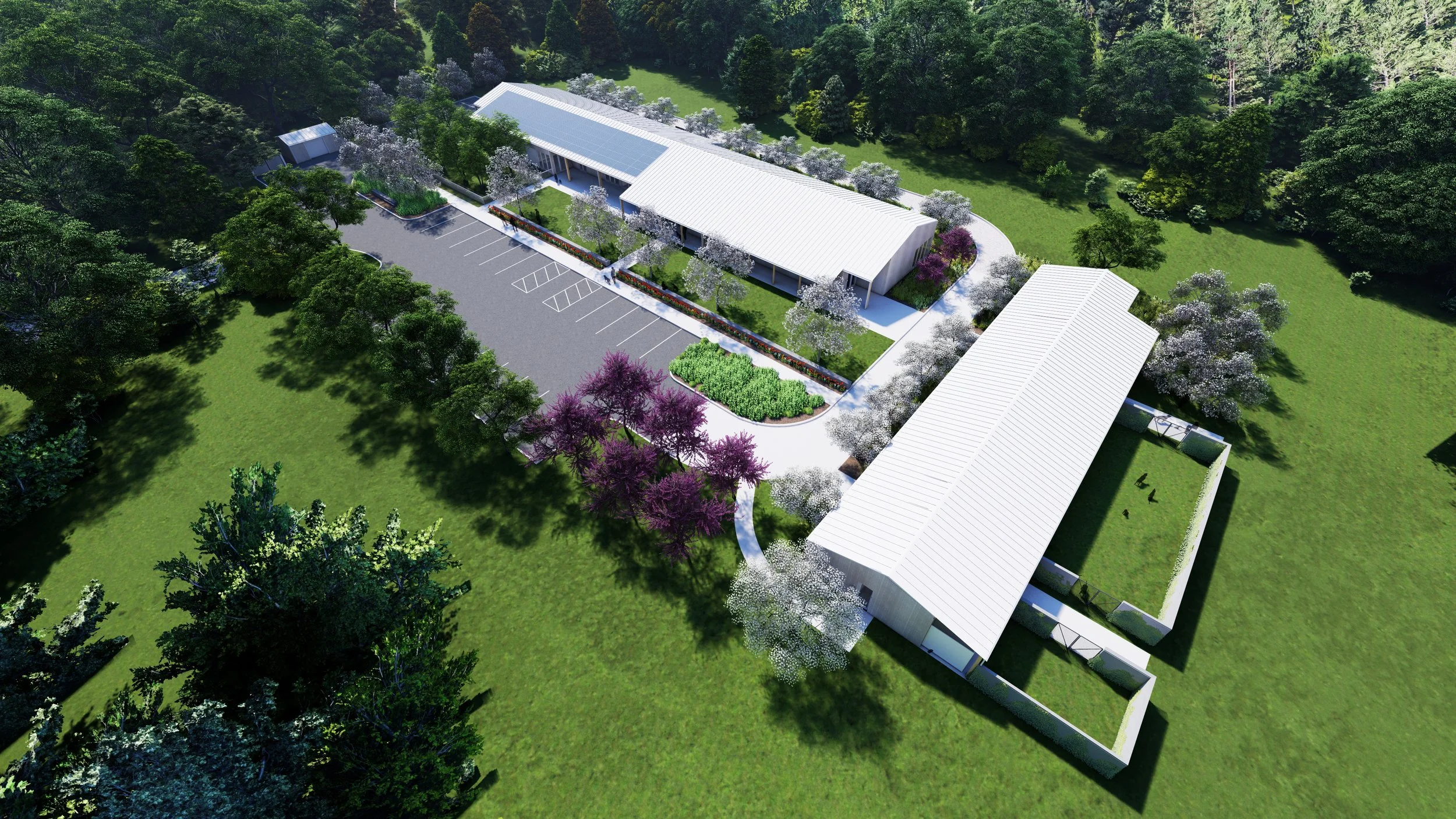 Aerial view of a modern building complex surrounded by greenery, trees with white and purple blossoms, a parking lot, and landscaped garden areas.