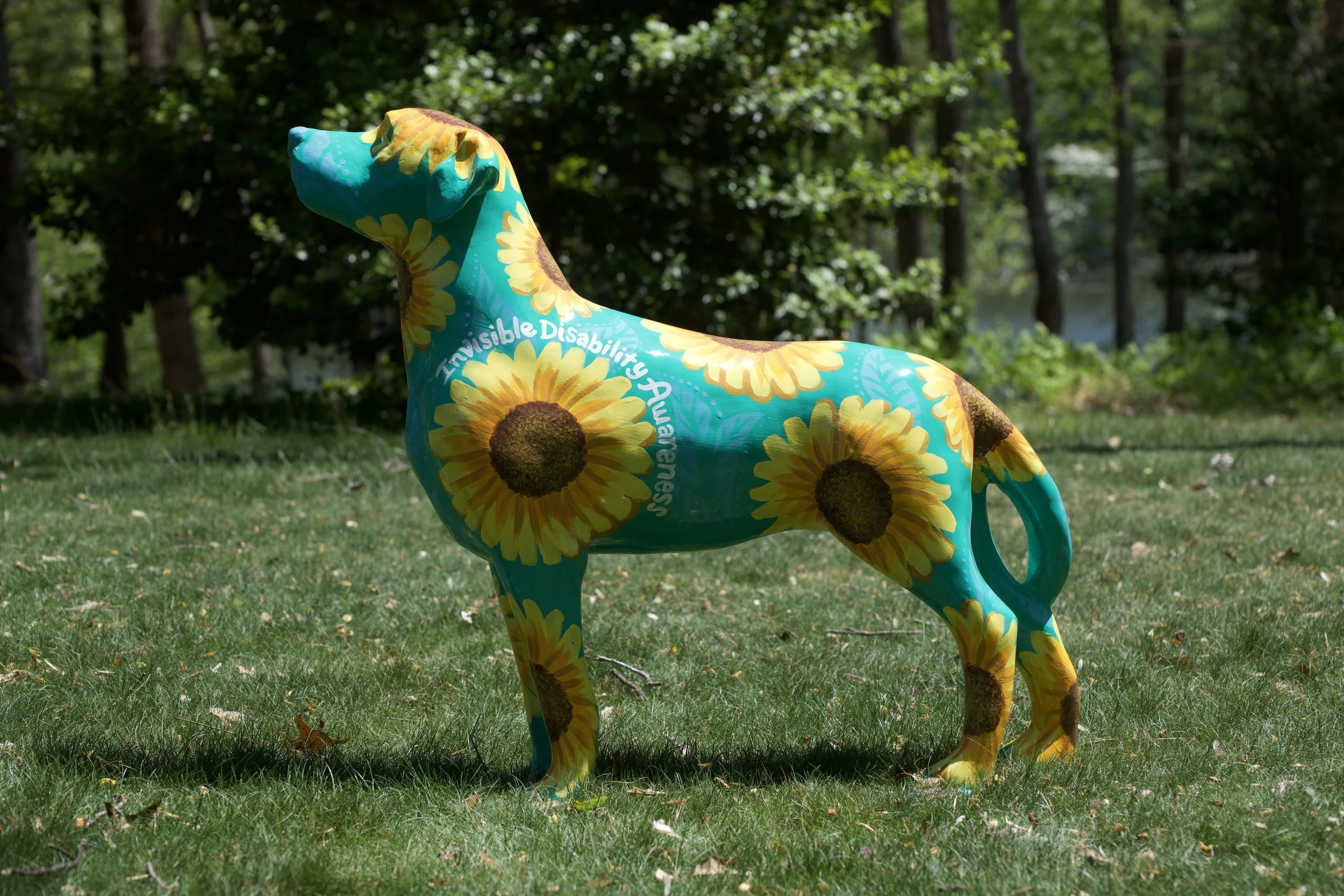 Colorful inflatable sculpture of a dog with sunflower designs, situated on a grassy area with trees in the background.