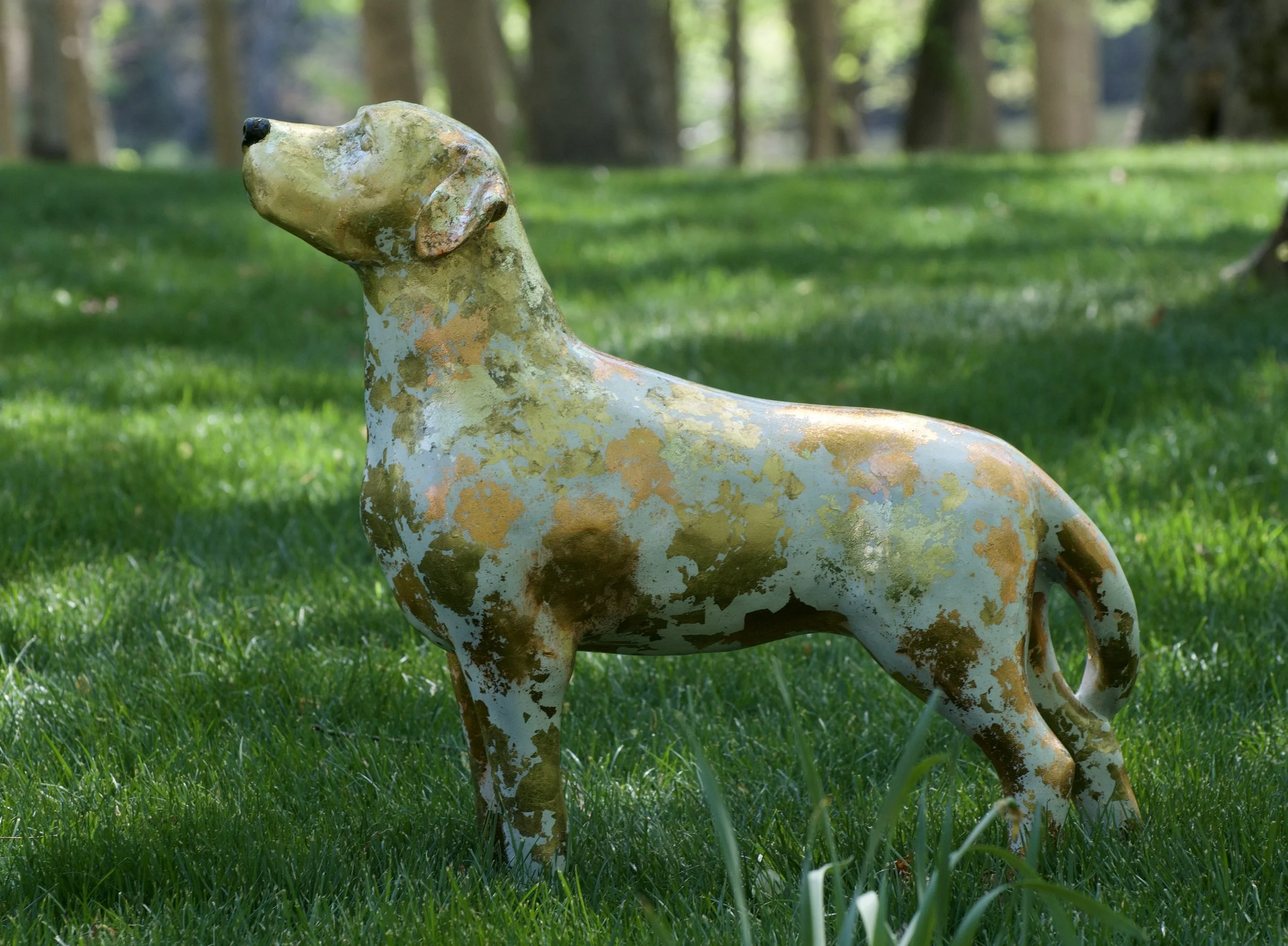 A weathered, painted metal horse sculpture outdoors on a grassy lawn with trees in the background.