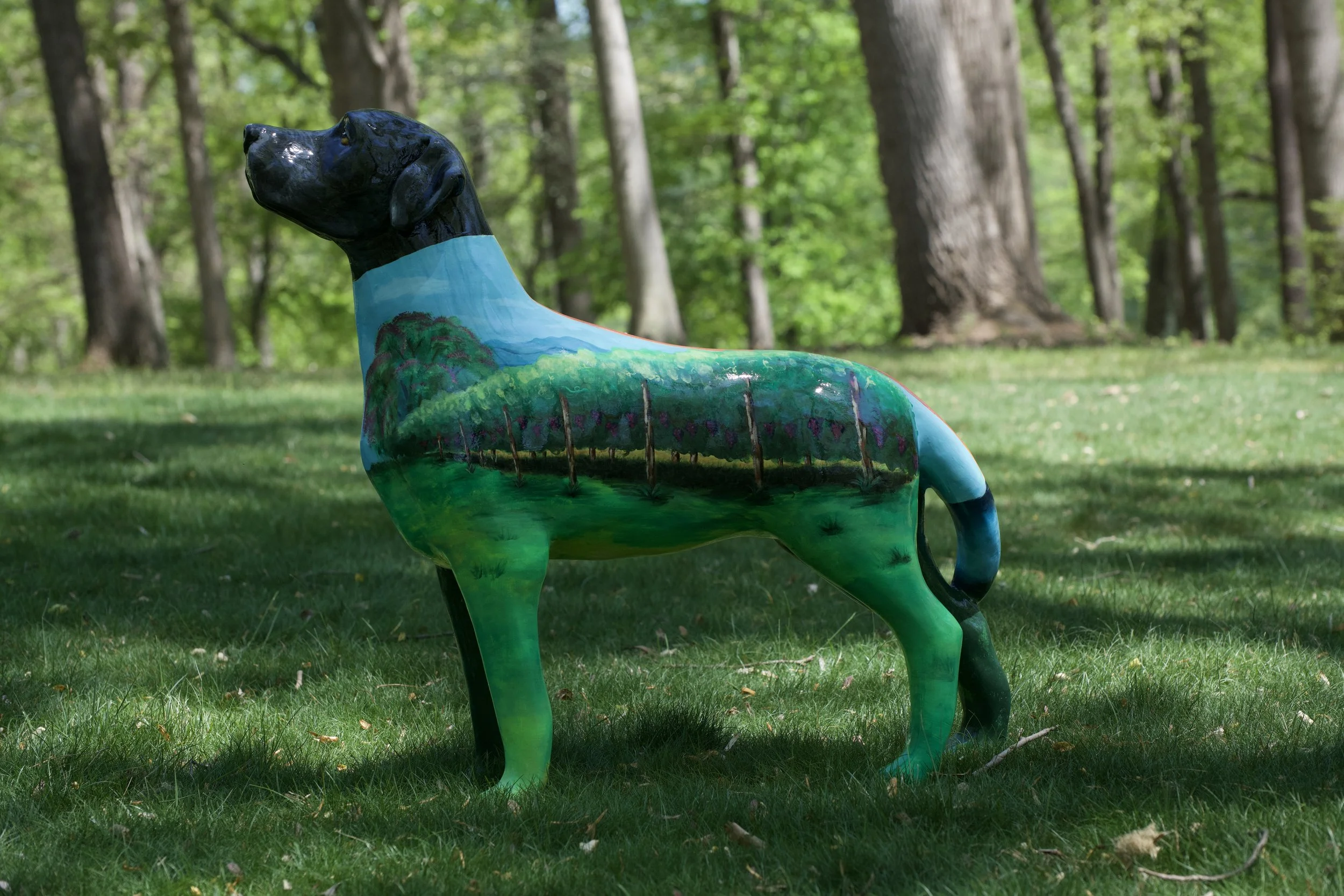 Colorful painted horse sculpture outdoors on grassy ground with trees and green foliage in the background.